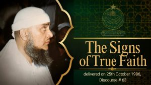 A bearded Muslim religious scholar wearing a white cap and white clothing, shown in side profile among people at an indoor gathering.